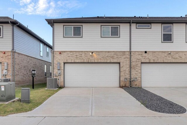 view of front of house with an attached garage, central AC unit, concrete driveway, and brick siding