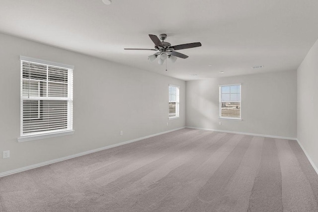 empty room with light colored carpet, a ceiling fan, and baseboards