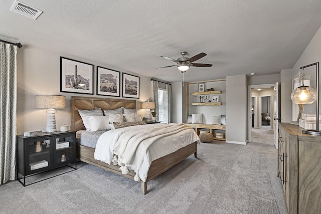 bedroom featuring light colored carpet, ceiling fan, visible vents, and a textured ceiling