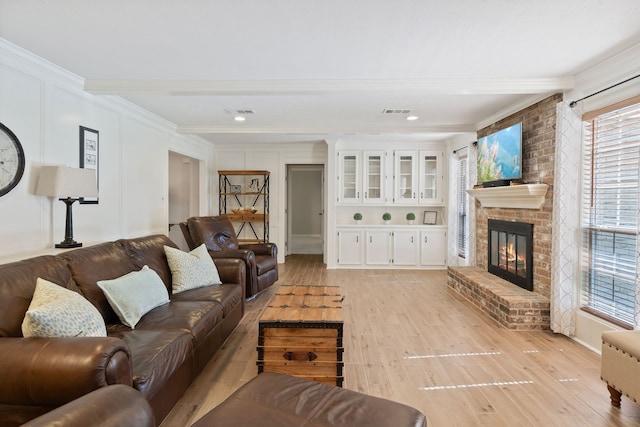 living room with visible vents, beam ceiling, a fireplace, and light wood finished floors