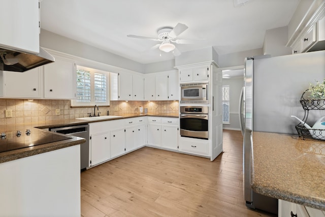 kitchen with a sink, appliances with stainless steel finishes, white cabinetry, light wood-type flooring, and backsplash