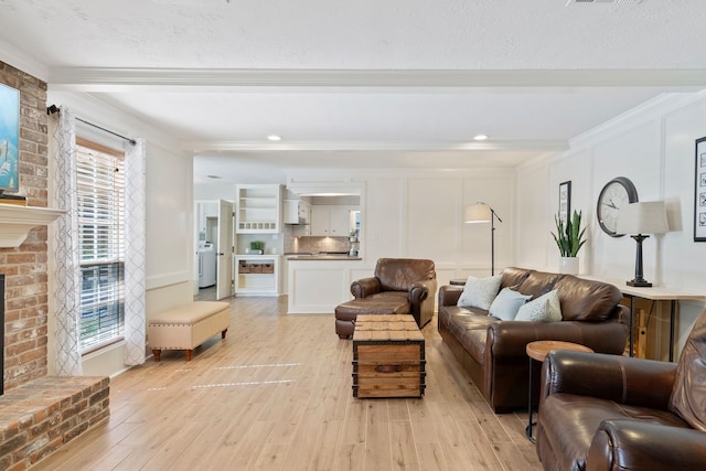 living room featuring beam ceiling, light wood-style flooring, washer / clothes dryer, a fireplace, and crown molding