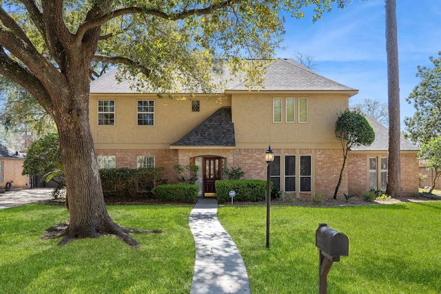 view of front of house with a front yard, brick siding, roof with shingles, and stucco siding