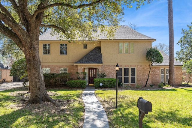 view of front of property with brick siding, stucco siding, a front lawn, and roof with shingles