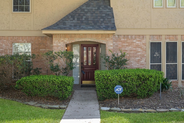 entrance to property featuring stucco siding, brick siding, and roof with shingles