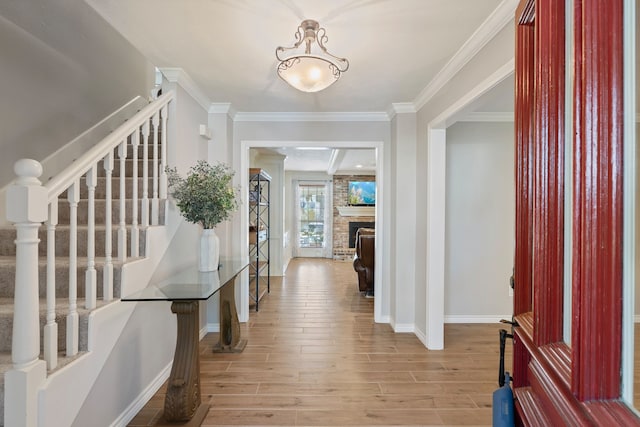 foyer entrance with a fireplace, baseboards, light wood-style floors, and ornamental molding