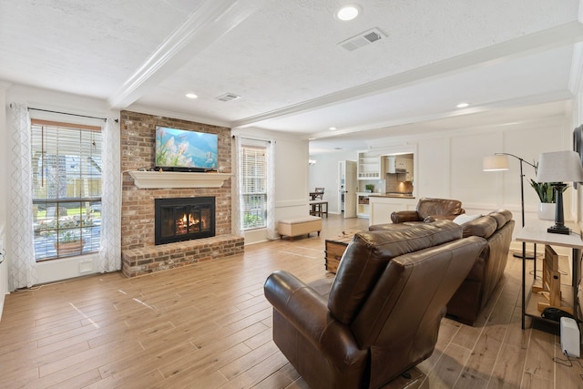 living area with beamed ceiling, a textured ceiling, visible vents, and light wood finished floors