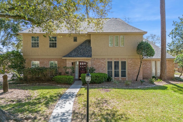 view of front facade featuring stucco siding, brick siding, roof with shingles, and a front yard