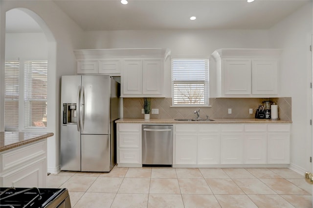 kitchen featuring arched walkways, light tile patterned flooring, stainless steel appliances, a sink, and decorative backsplash