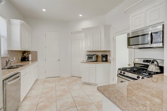 kitchen featuring white cabinets, light stone counters, stainless steel appliances, and a sink