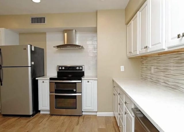 kitchen featuring visible vents, white cabinets, stainless steel appliances, light wood-type flooring, and wall chimney range hood