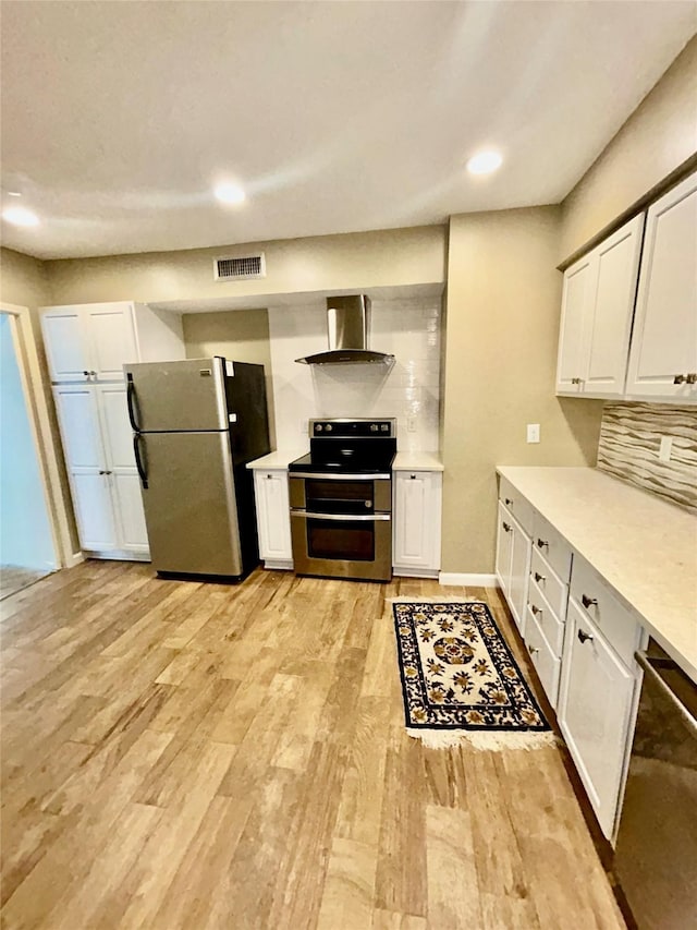 kitchen with white cabinetry, light wood-style floors, appliances with stainless steel finishes, decorative backsplash, and wall chimney exhaust hood