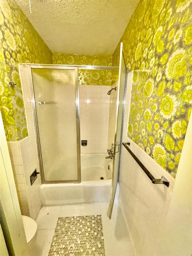 full bathroom with a wainscoted wall, tile walls, wallpapered walls, a textured ceiling, and tile patterned floors