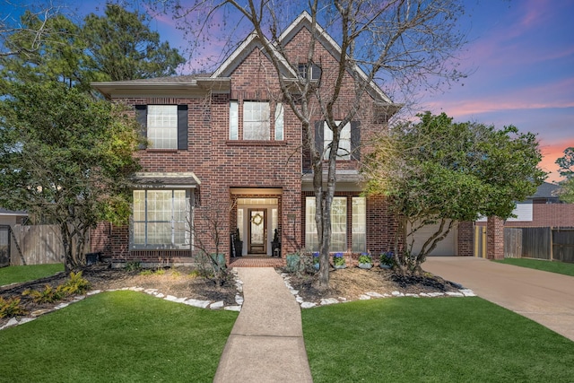 traditional home with concrete driveway, brick siding, a lawn, and fence