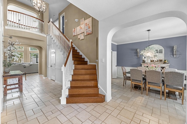 stairs with arched walkways, ornamental molding, a high ceiling, french doors, and a chandelier