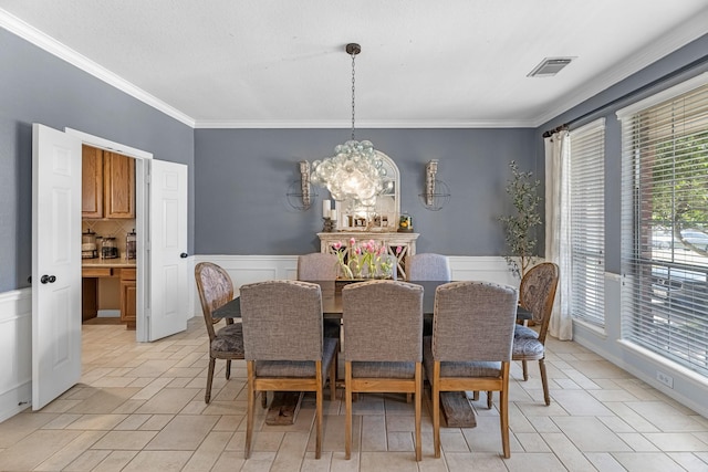 dining space with ornamental molding, visible vents, a chandelier, and wainscoting