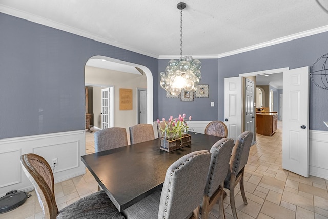 dining space featuring a wainscoted wall, arched walkways, a notable chandelier, and ornamental molding