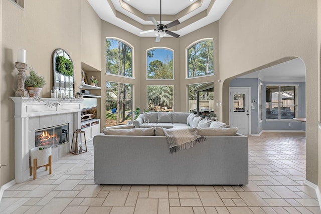 living area featuring a ceiling fan, plenty of natural light, arched walkways, and a tiled fireplace