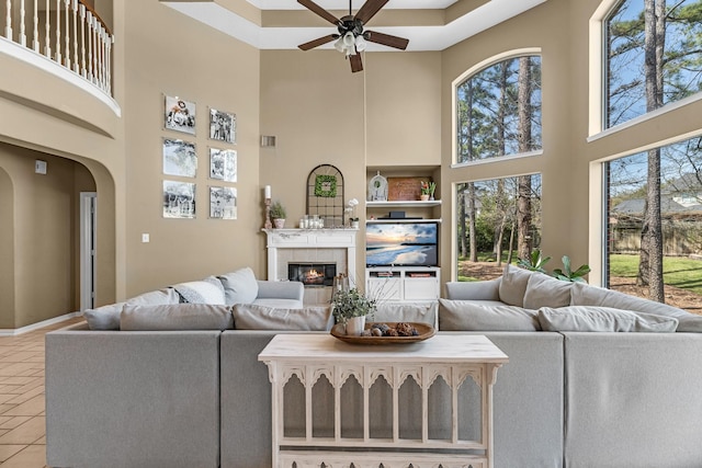 living room featuring arched walkways, ceiling fan, tile patterned flooring, a high ceiling, and a tiled fireplace