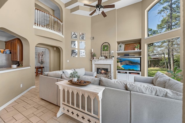 living room with arched walkways, a fireplace, stone tile floors, a ceiling fan, and baseboards