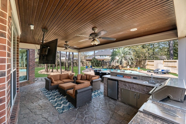 view of patio featuring an outdoor kitchen, a ceiling fan, fence, an outdoor living space, and a sink