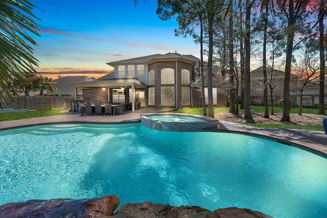 pool at dusk with a patio, outdoor dry bar, a pool with connected hot tub, ceiling fan, and fence