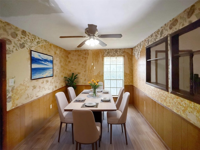 dining space featuring wainscoting, ceiling fan, light wood finished floors, and wallpapered walls