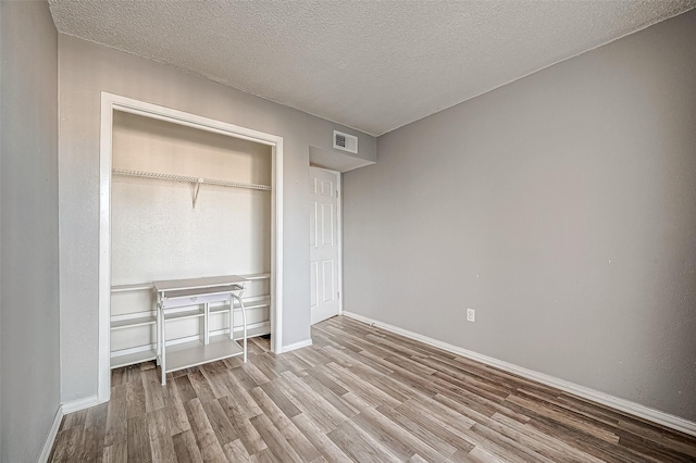 unfurnished bedroom with visible vents, a textured ceiling, baseboards, and wood finished floors