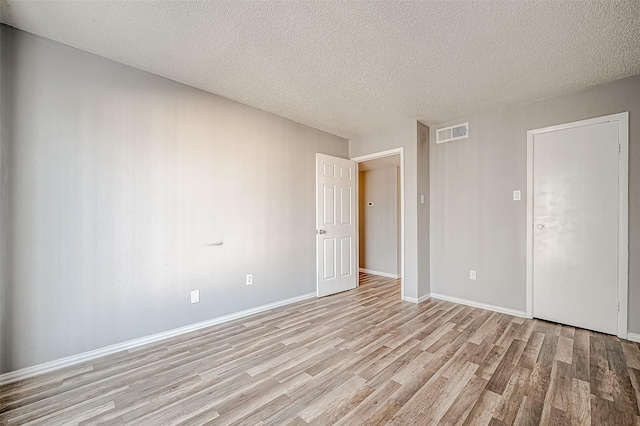 unfurnished bedroom featuring a textured ceiling, light wood-style flooring, visible vents, and baseboards