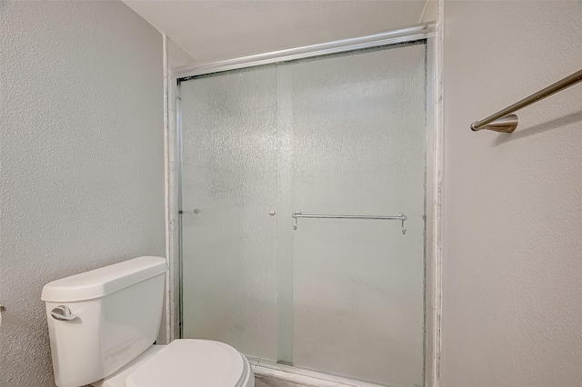 bathroom featuring a stall shower, a textured wall, and toilet