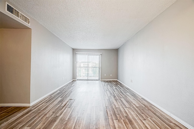 unfurnished room with visible vents, a textured ceiling, baseboards, and wood finished floors