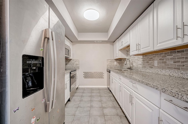 kitchen featuring a tray ceiling, appliances with stainless steel finishes, white cabinetry, a sink, and light stone countertops