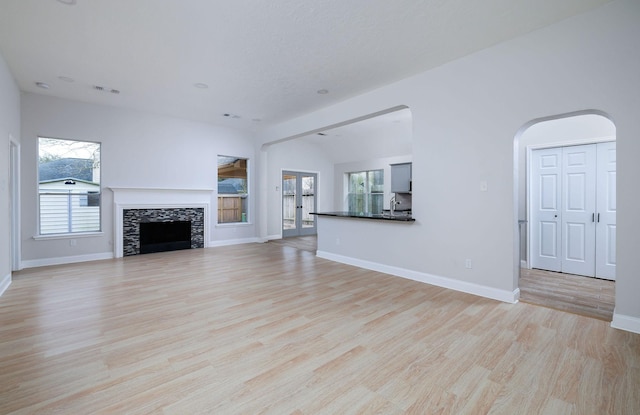 unfurnished living room with arched walkways, baseboards, visible vents, light wood-style flooring, and a fireplace