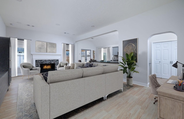 living area featuring a warm lit fireplace, visible vents, arched walkways, baseboards, and light wood-style floors