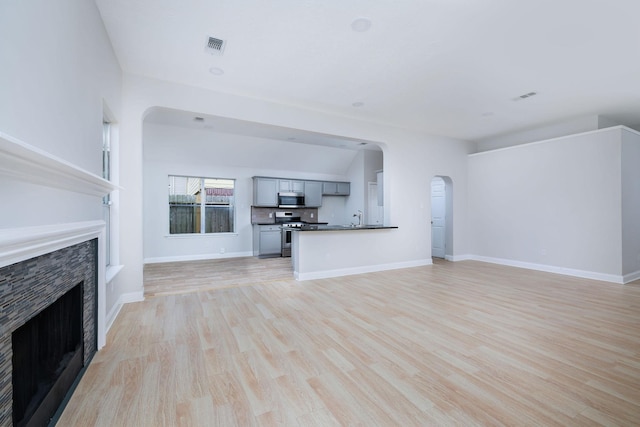 unfurnished living room with arched walkways, a fireplace, light wood-style flooring, and baseboards