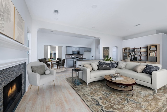 living area featuring arched walkways, a lit fireplace, visible vents, and light wood-style flooring