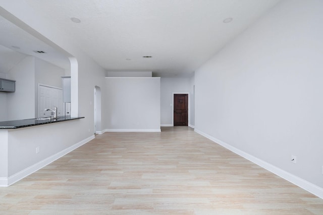 unfurnished living room with light wood-style floors, arched walkways, visible vents, and baseboards