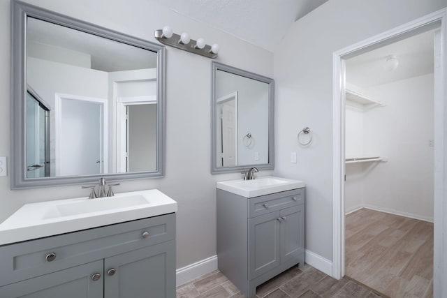 bathroom featuring a spacious closet, wood finished floors, two vanities, and a sink