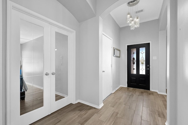 foyer entrance with visible vents, light wood finished floors, an inviting chandelier, arched walkways, and french doors