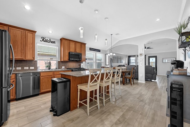 kitchen with a kitchen island, open floor plan, arched walkways, appliances with stainless steel finishes, and lofted ceiling