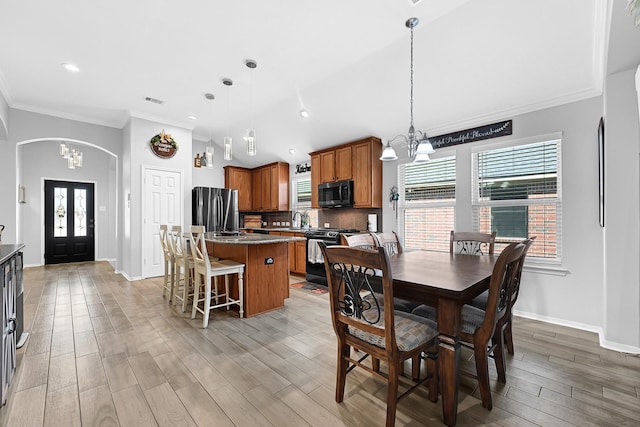 dining space featuring light wood-type flooring, arched walkways, baseboards, and crown molding