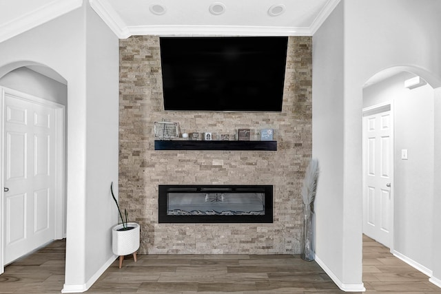 living room featuring crown molding, baseboards, wood tiled floor, arched walkways, and a glass covered fireplace