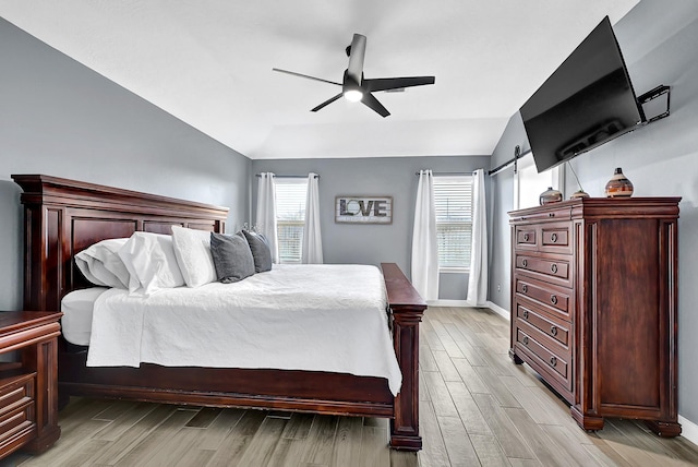 bedroom with baseboards, light wood-type flooring, multiple windows, and lofted ceiling