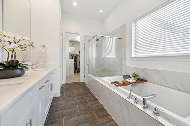 full bath featuring double vanity, a sink, a shower stall, a walk in closet, and a garden tub