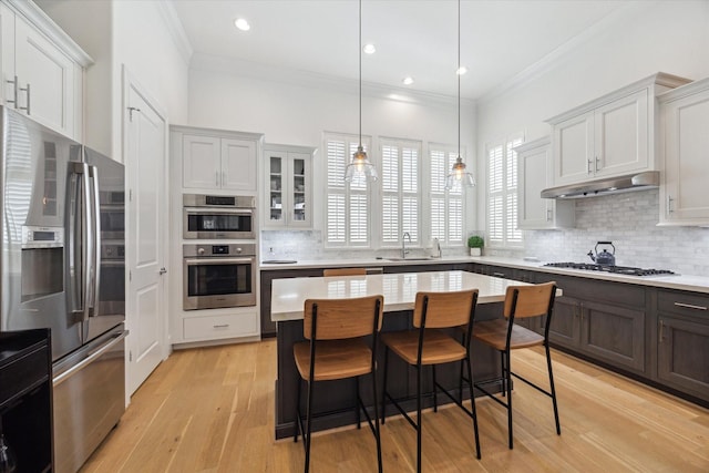 kitchen featuring under cabinet range hood, stainless steel appliances, tasteful backsplash, and light countertops