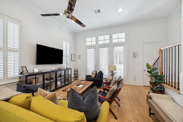 living area with light wood-type flooring, visible vents, ornamental molding, ceiling fan, and stairs