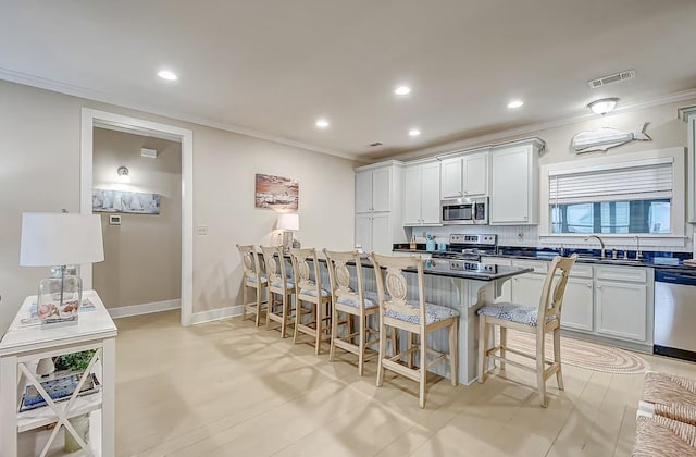 kitchen featuring a breakfast bar, stainless steel appliances, visible vents, ornamental molding, and a sink