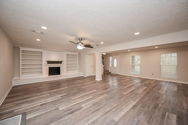 unfurnished living room featuring visible vents, stairway, wood finished floors, a textured ceiling, and a fireplace