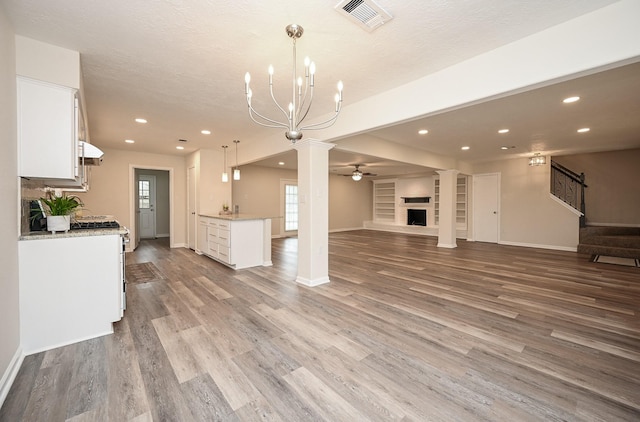 unfurnished living room featuring decorative columns, visible vents, a fireplace with raised hearth, light wood-style flooring, and stairs