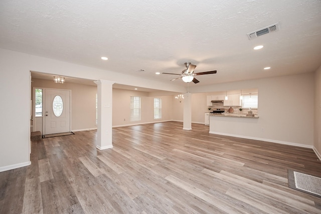 unfurnished living room with visible vents, decorative columns, light wood-style flooring, and baseboards